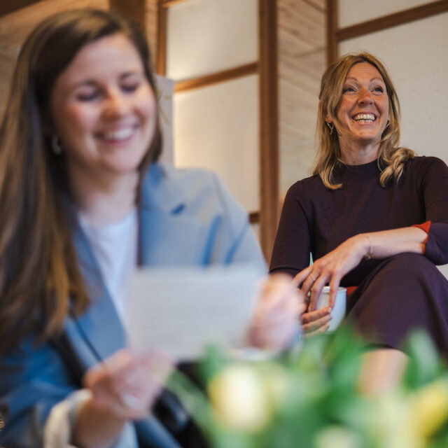 Bild im Rahmen von Framechangers™. Zwei Frauen lachen, die eine hält eine Tasse, die andere eine Notiz.