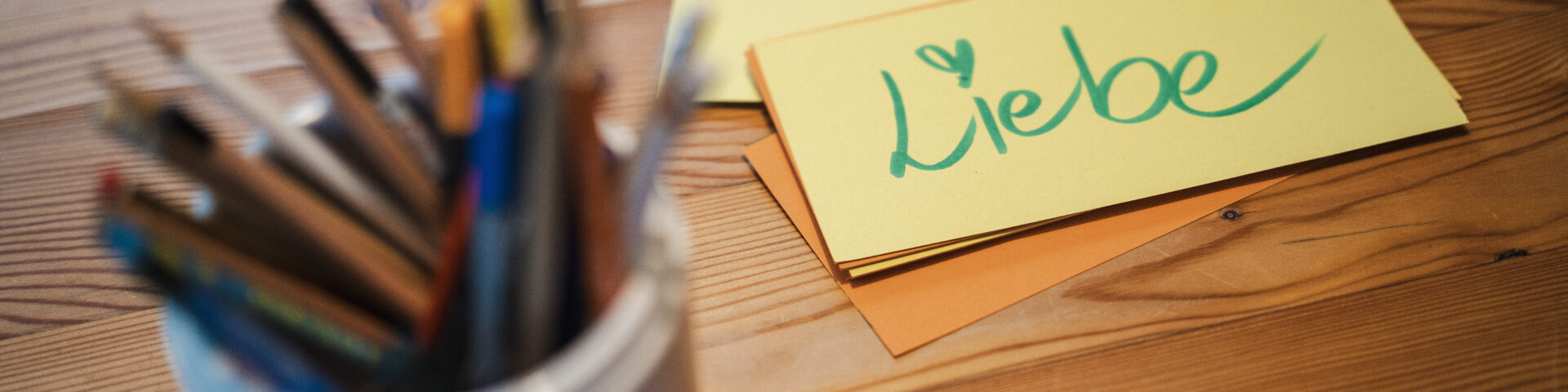 Framechangers™ Inspiration: Bunte Stifte und gelbe Karte mit der Aufschrift Liebe auf einem Holztisch.