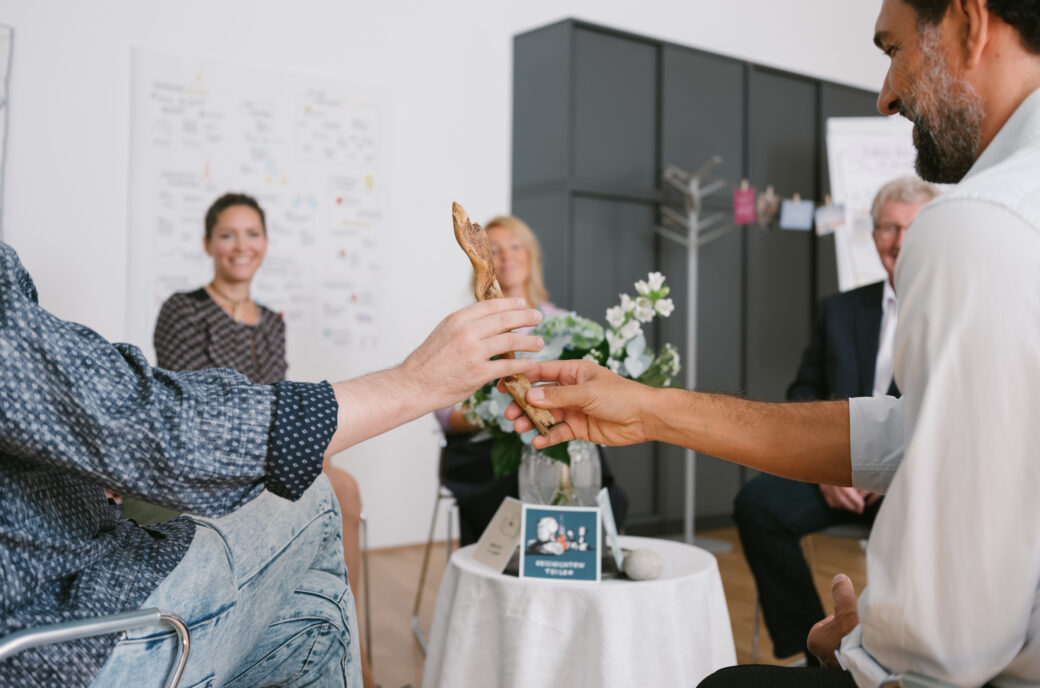 Menschen sitzen im Kreis und reichen sich während eines Mindful-Leadership-Treffens ein Holzstück.