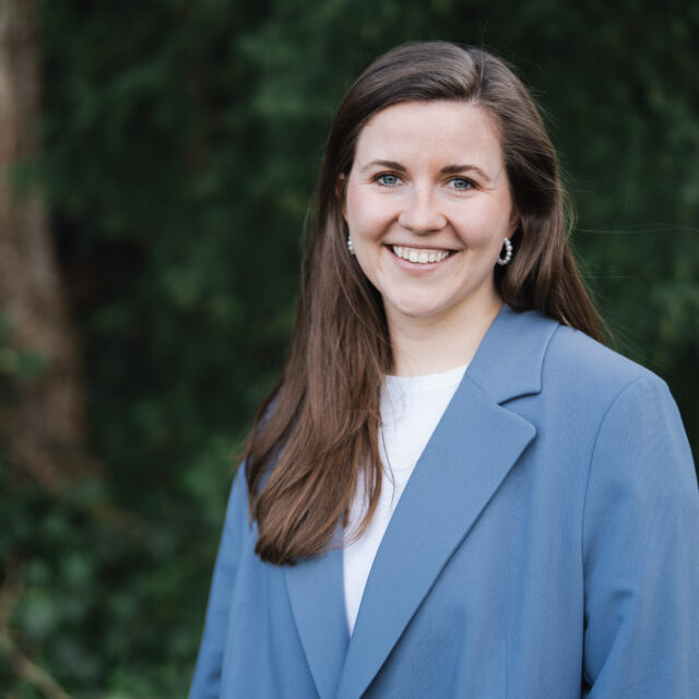 Liese, Mindful Leadership Coach von Framechangers™ Elisabeth Kraus, lächelt in einem blauen Blazer vor grünem Hintergrund.