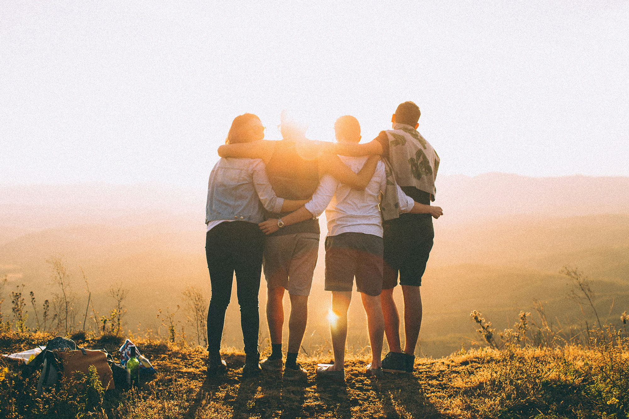 Vier Freunde umarmen sich und blicken auf einen sonnigen Horizont.