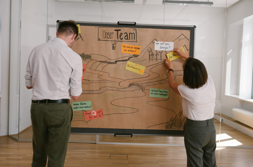 Zwei Personen arbeiten an einer Tafel mit der Aufschrift "Unser Team" für Inside Out Leadership Coaching.