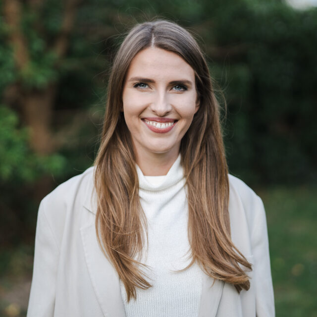 Porträt von Anna, einem achtsamen Leadership Coach, mit einem strahlenden Lächeln vor grünem Hintergrund.