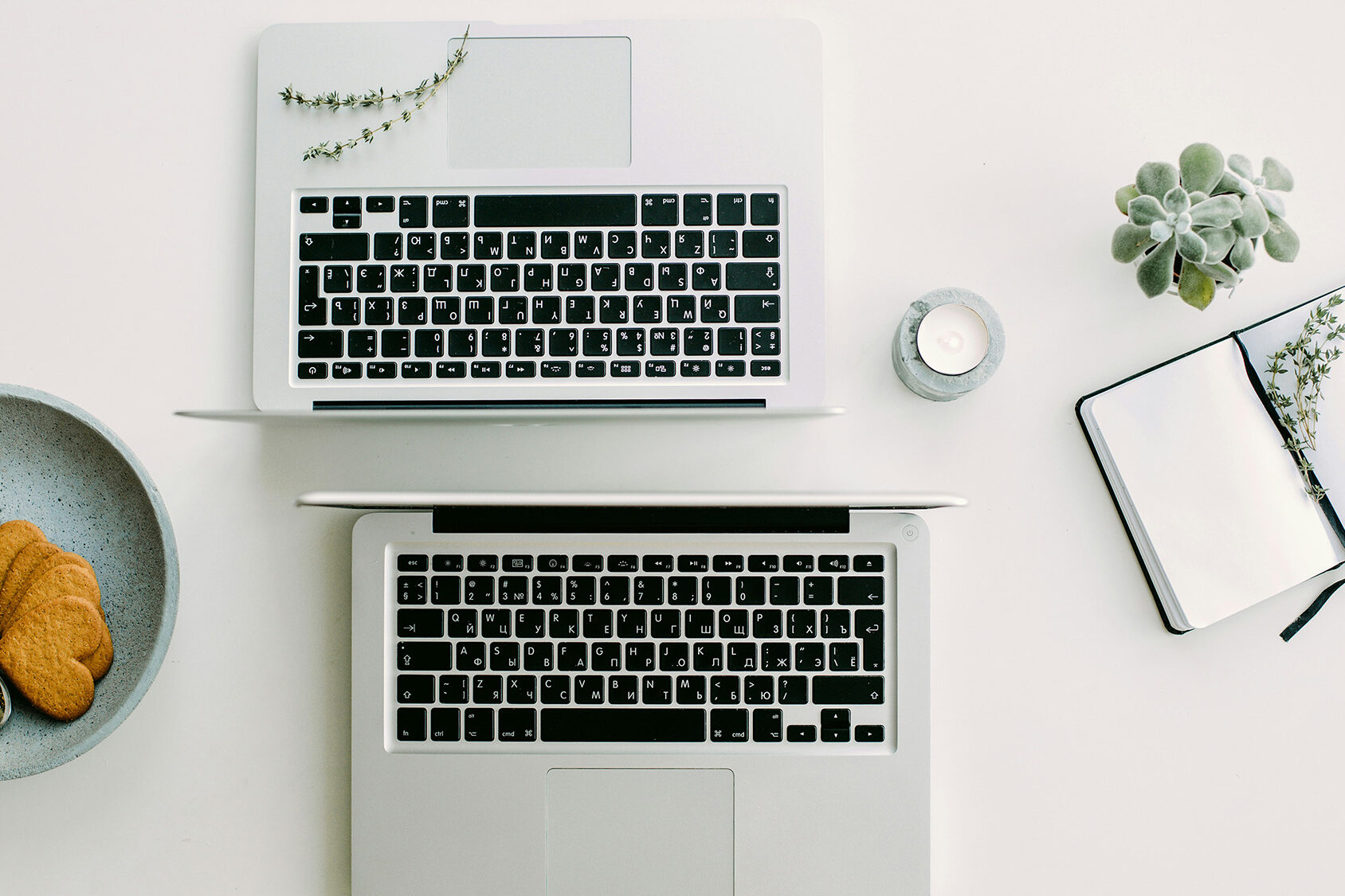Warum emotionale Intelligenz in der KI-Ära unverzichtbar bleibt Zwei Laptops, Notizbuch, Keks und Kerze auf weißem Tisch. Gedankenflüsse