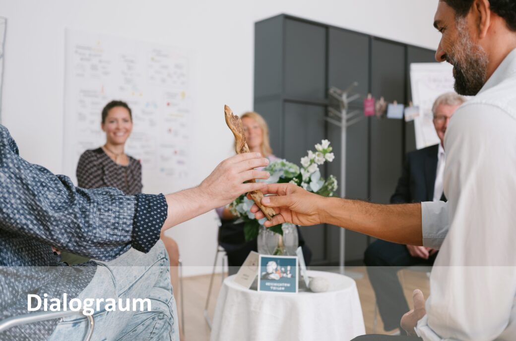 Personen tauschen sich in der Community aus und halten ein Stück Holz in der Hand.