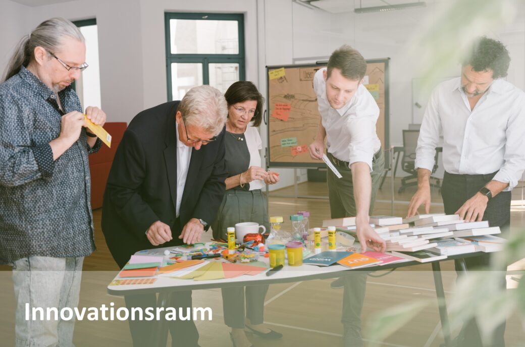 Eine Gruppe von Personen arbeitet gemeinsam im Innovationsraum an einem Tisch mit Bastelmaterialien.