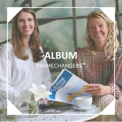 Zwei lächelnde Frauen sitzen an einem Tisch mit der Aufschrift Album Framechangers™.