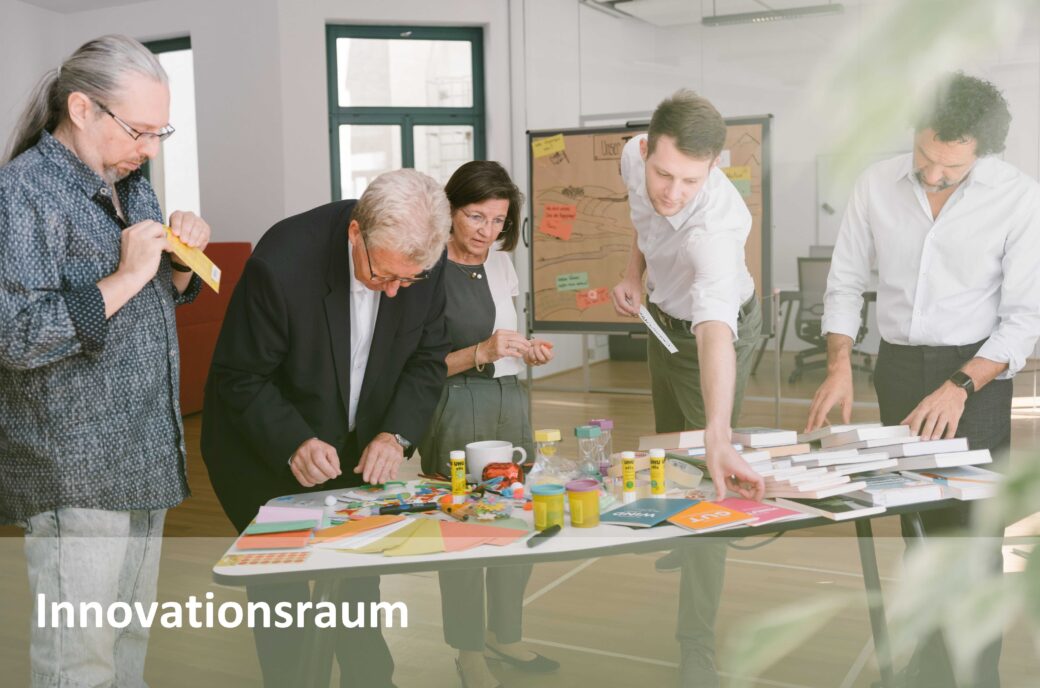 Menschen arbeiten an einem Tisch mit Bastelmaterialien; Text "Innovationsraum"